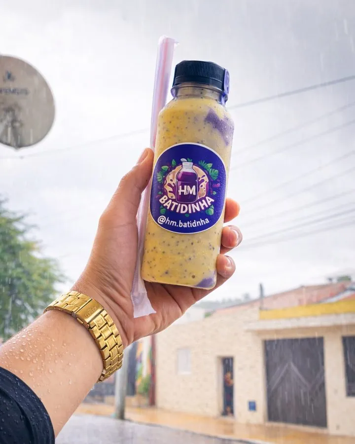 Garrafinha HM Batidinha de açaí com maracujá, segurada na mão em um dia de chuva (abre o Instagram)